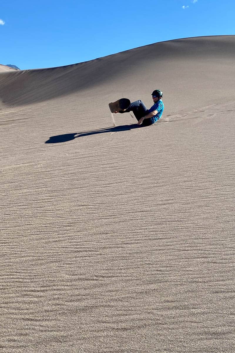 Man fallen on sand while sandboarding in Colorado Great Sand Dunes National Park.