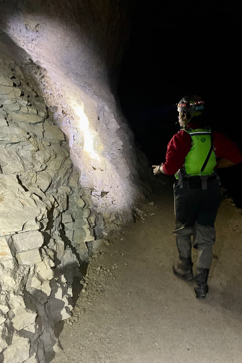 Tour guide in high-visibility vest pointing out features of rock wall in abandoned mine.