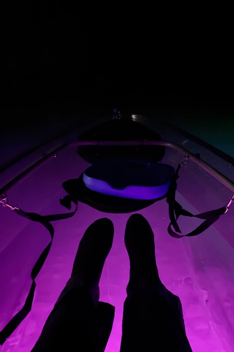 Silhouette of kayaker's feet in purple lit boat on underground lake.