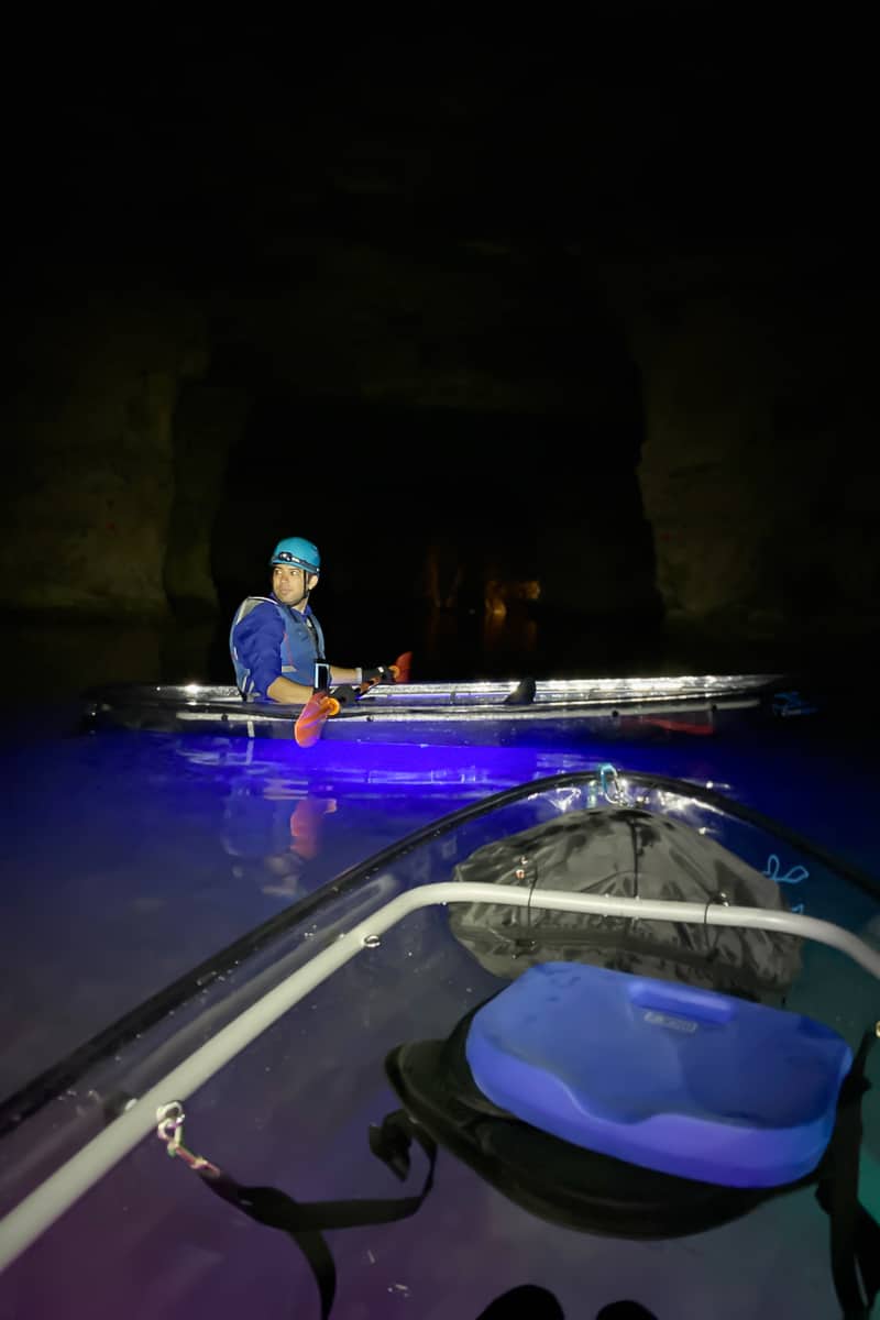 Kayaker in boat on blue lit underground lake.