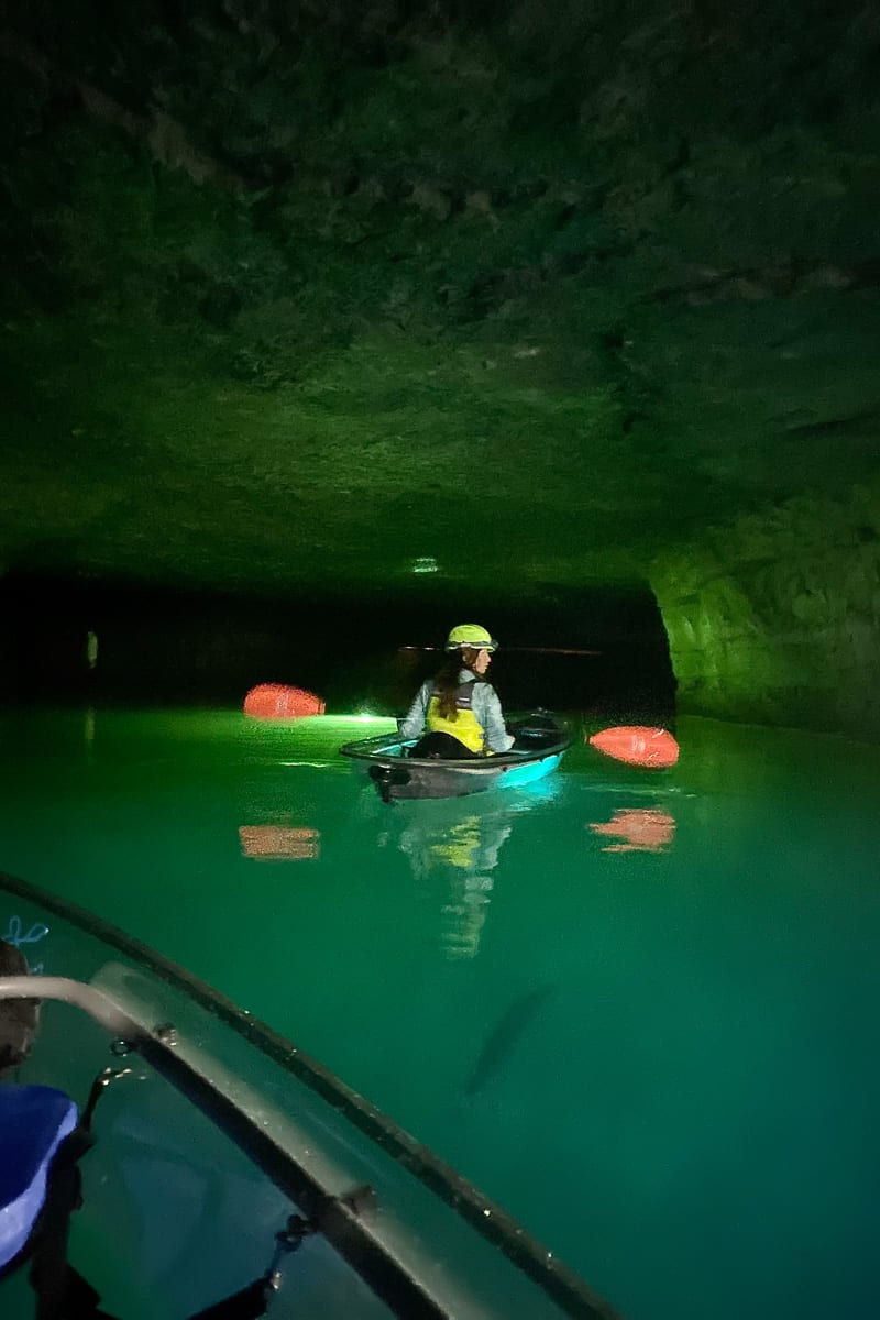 Kayaker in boat on green lit underground lake.