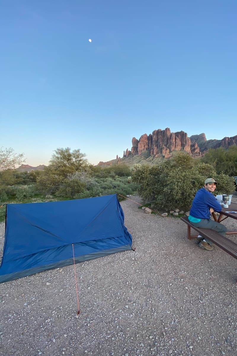 Man sitting at picnic table next to blue tent with tarp over it.