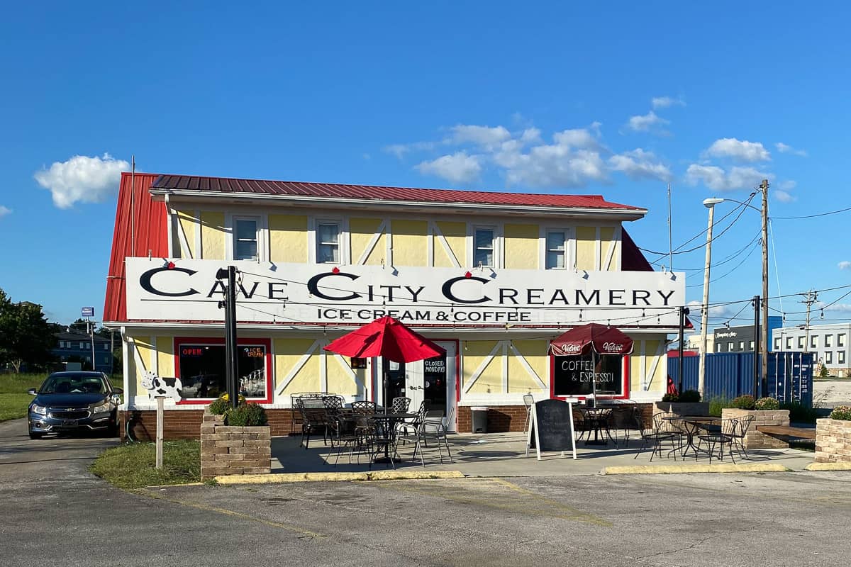 Yellow two-story building with chairs and tables outside and sign for Cave City Creamery.