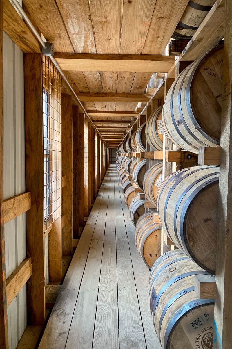 Long row of bourbon barrels stacked inside rickhouse.