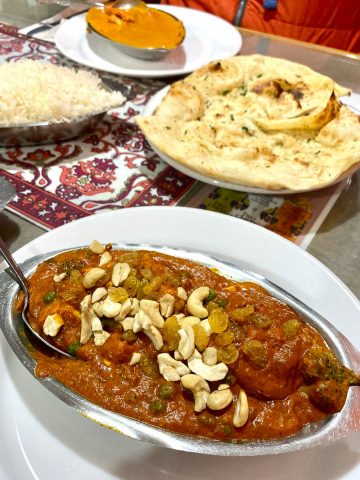 Navratan korma with naan, rice, and chicken tikka masala in background.