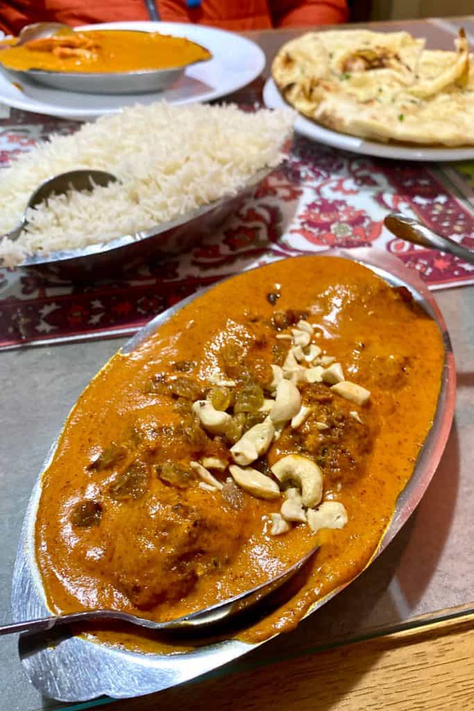 Malai kofta with garlic naan, rice, and chicken tikka masala in background.