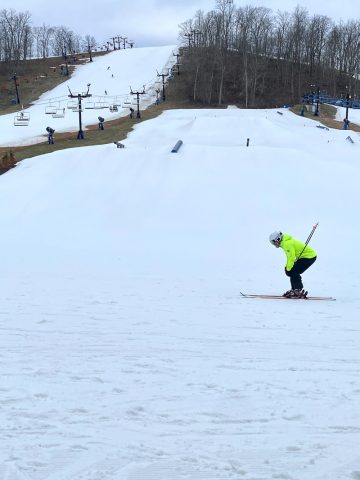 Skier in neon yellow coat at bottom of snowy run.
