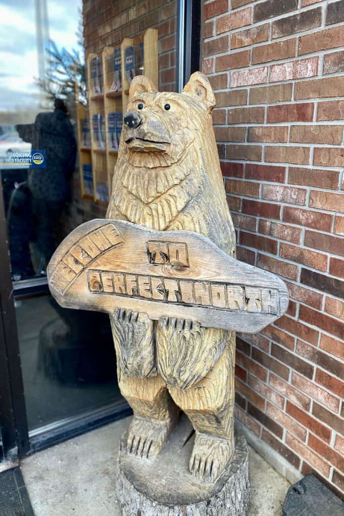 Carved wooden bear holding sign that says "Welcome to Perfect North."