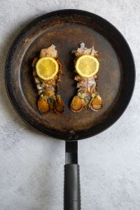 lobster tails in a pan, topped with lemon.