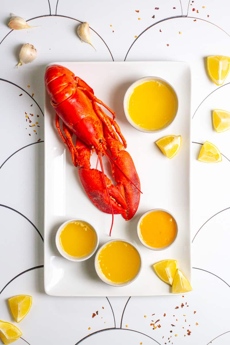 lobster on a platter with butter sauce, lemon wedges + garlic