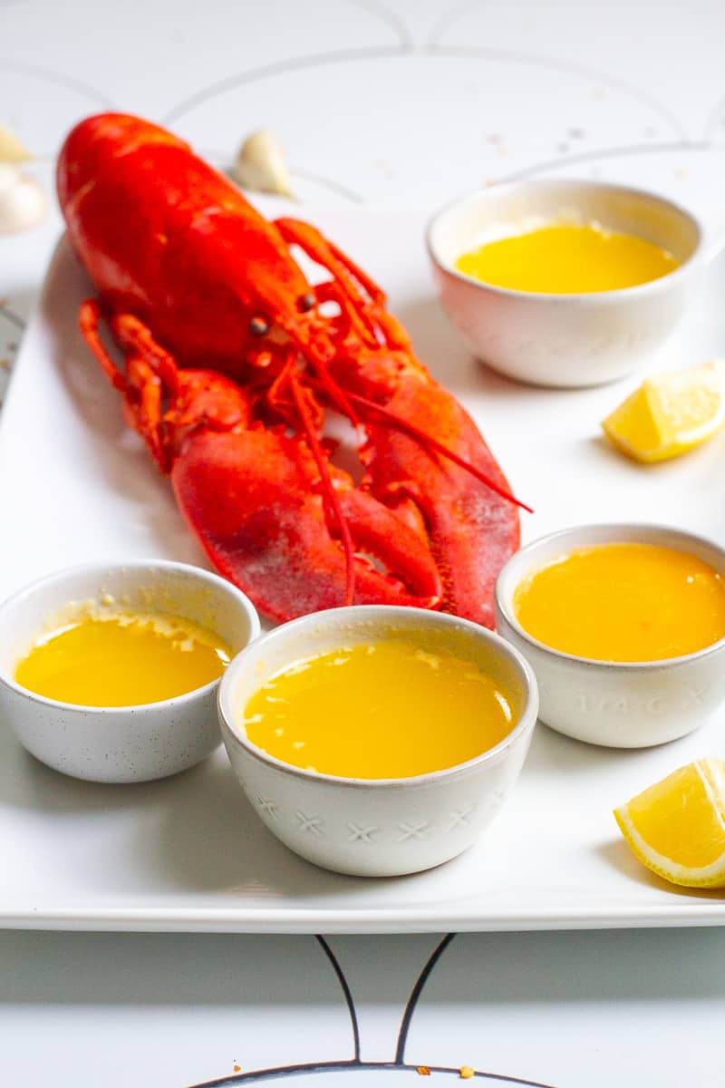 lobster on a platter with butter sauce, lemon wedges + garlic