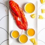 lobster on a platter with butter sauce, lemon wedges + garlic