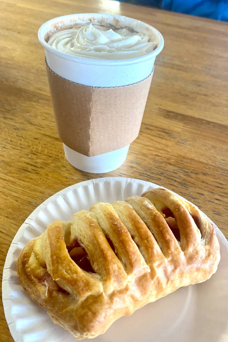 Latte in paper cup next to fruit pastry.