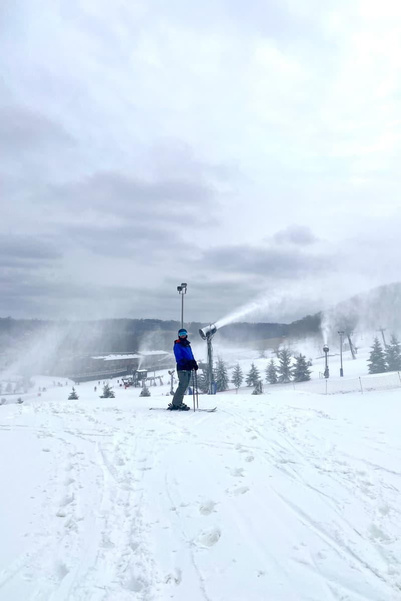 Skier with goggles stopped at top of hill with snow blowing around him.