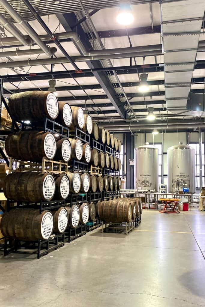 Stacked whiskey barrels with large tanks in background at Lexington Brewing & Distilling Co.