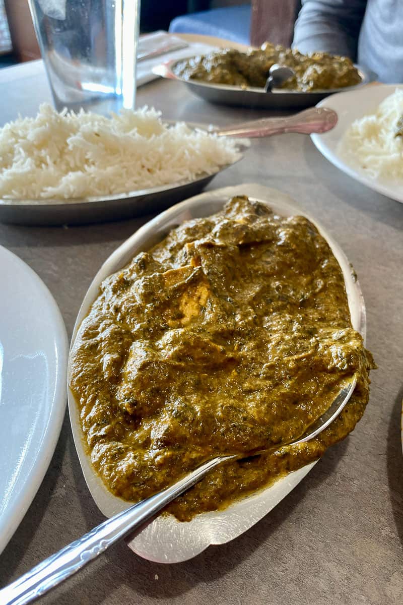 Dish of chicken tikka saag, with dish of rice and dish of chicken saag in background.