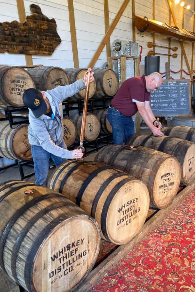 People using whiskey thief to fill bottles from the barrel.