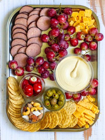 Camp charcuterie board with fruit, crackers, nuts, olives, sausage rounds, cheese and hummus.