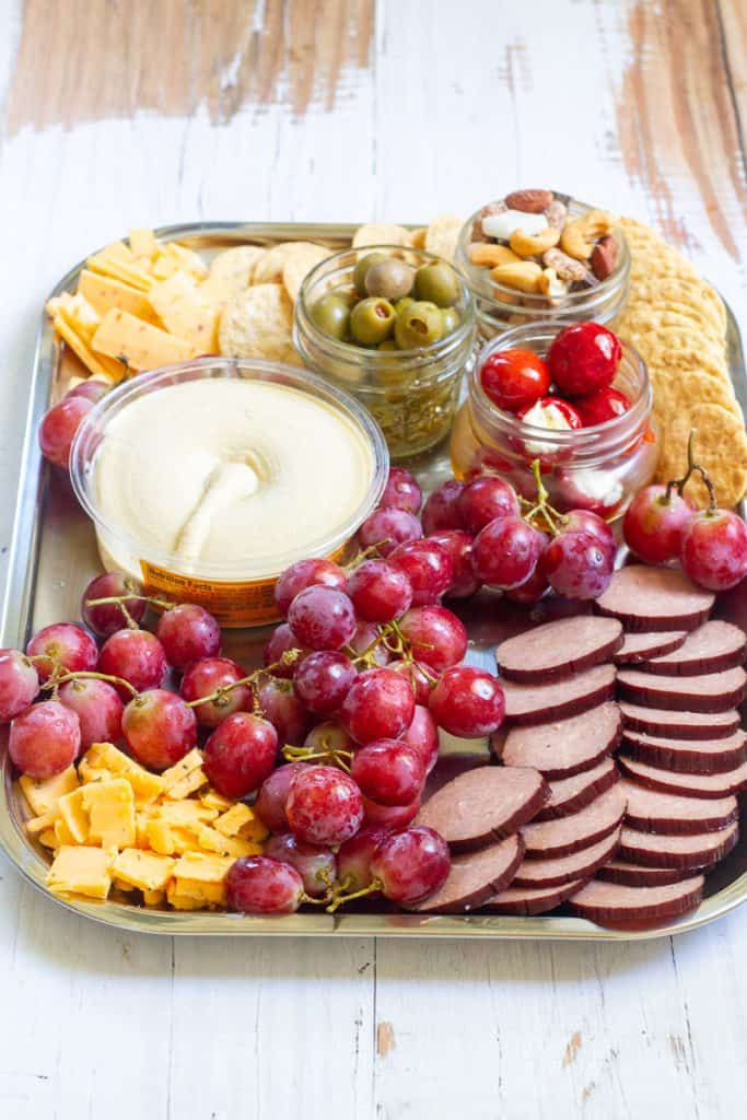 Camping charcuterie board with fruit, crackers, nuts, olives, sausage rounds, cheese and hummus.