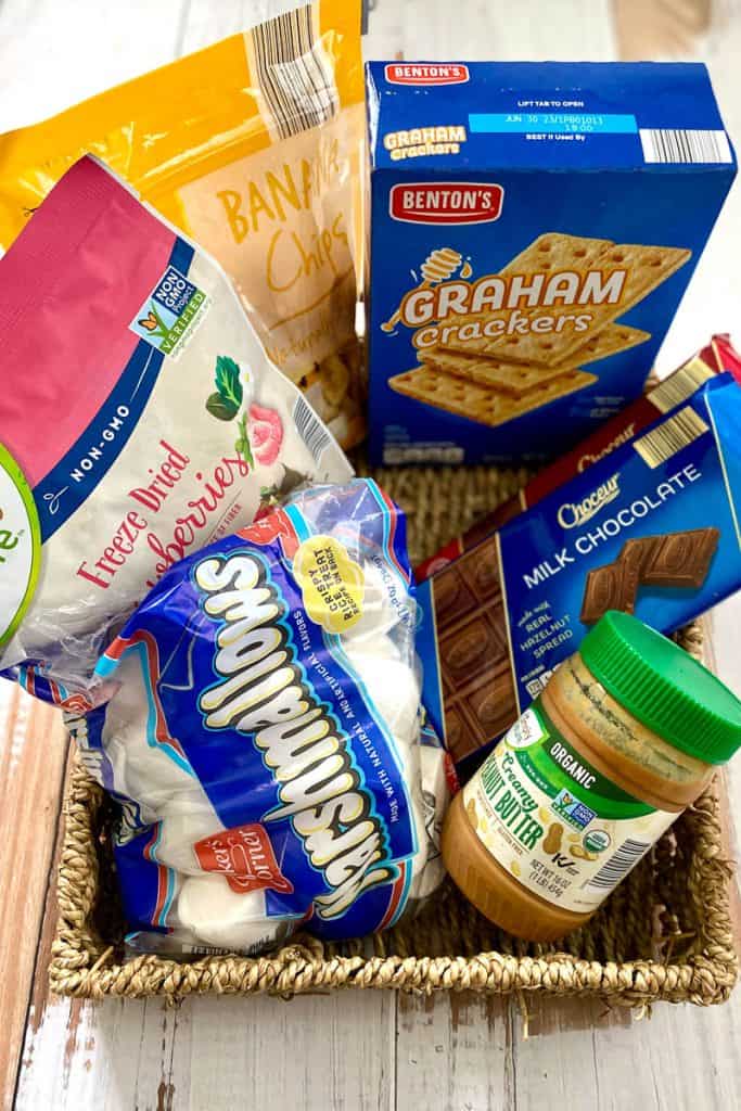 Packages of marshmallows, peanut butter, chocolate, and dried fruit in basket.