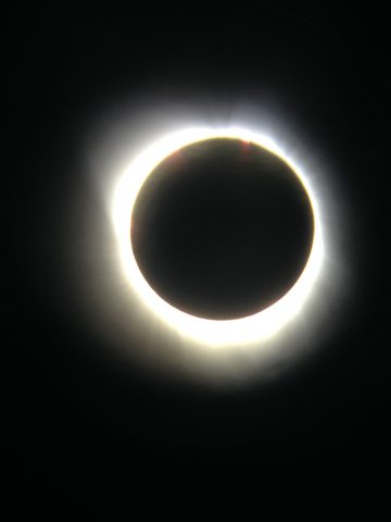 Solar eclipse as seen in the path of totality, with moon completely covering sun and light streaming out from behind it.