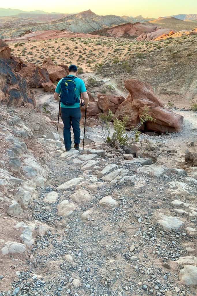 Hiker with trekking poles descending rocky path on Fire Wave Trail.