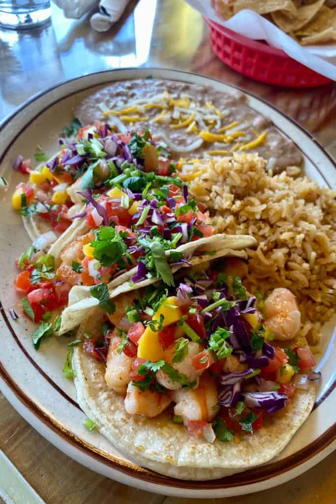 Shrimp tacos with rice and beans on plate.
