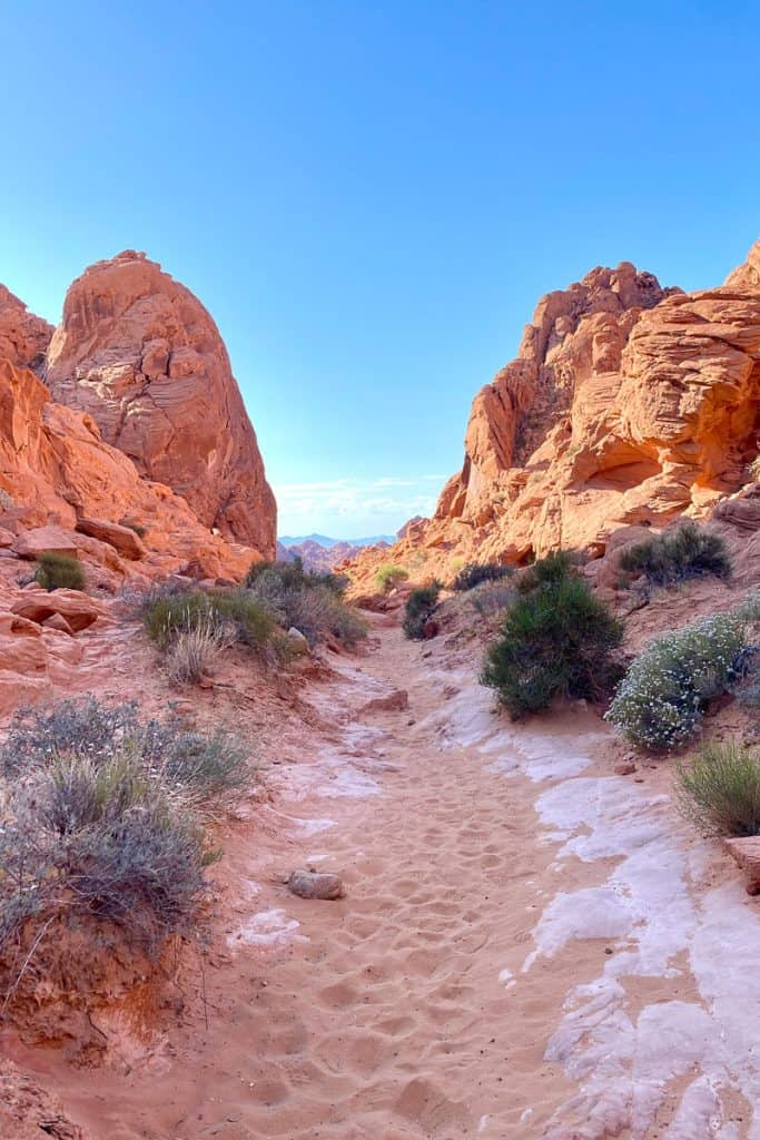 Sandy path with large red rock formations on either side.