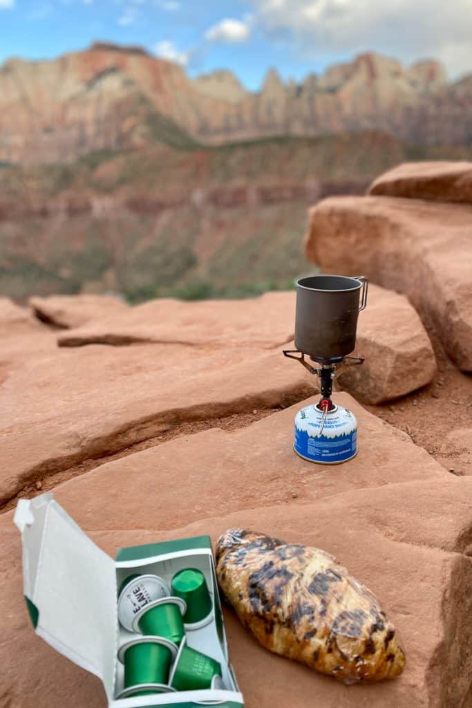 Espresso pods, chocolate croissant, and small gas burner set on red rock.