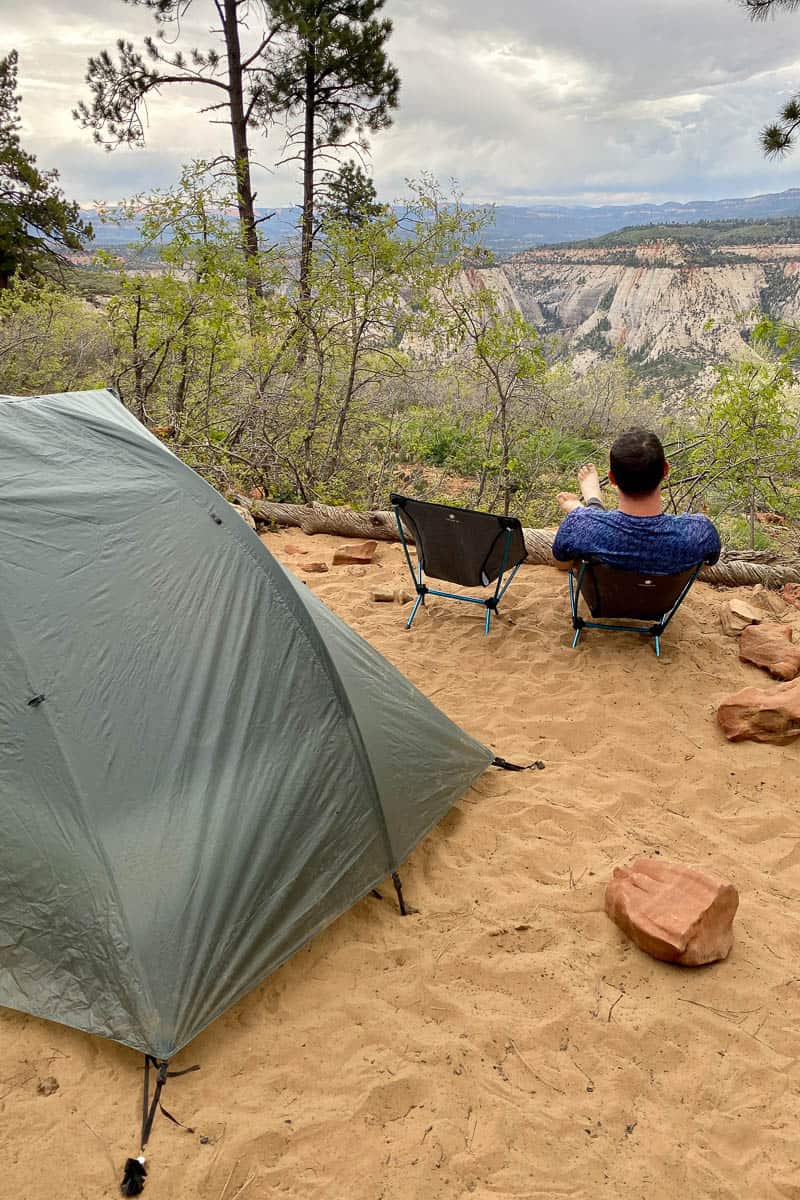 Man sitting in camp chair next to tent observing view of canyon.