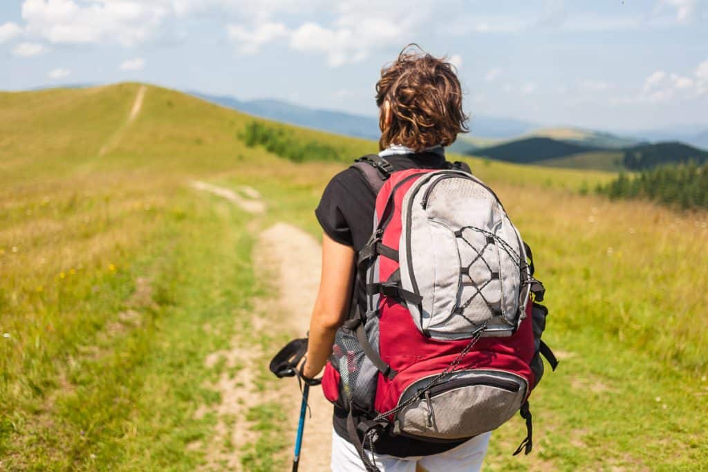Woman wearing backpacking pack for petite women walking on flat grassy trail.