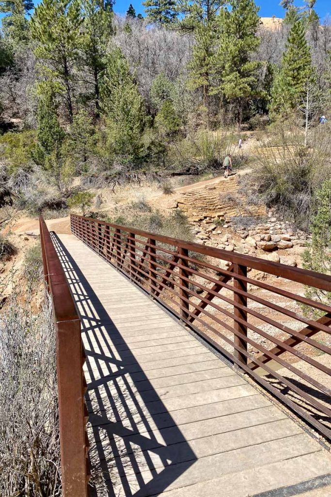 Wooden bridge with metal railings crossing gully.