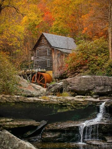Glade Creek Grist Mill with waterfall in front surrounded by yellow- and red-leaved trees.