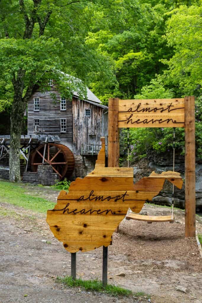 Wooden carving of state of West Virginia with words "almost heaven" in front of Glade Creek grist mill.