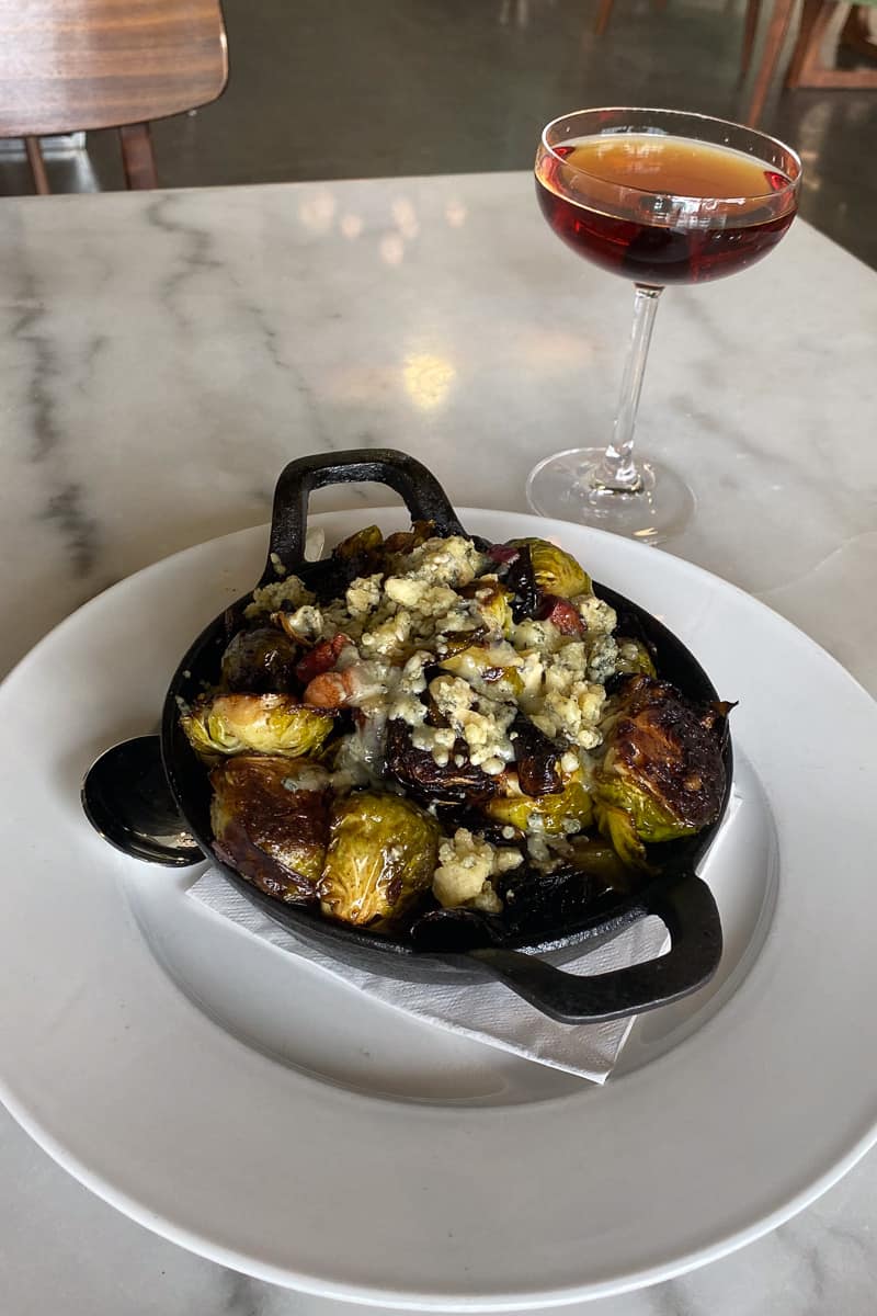 Brussels sprouts with maple glaze, blue cheese, and bacon served in cast-iron dish.