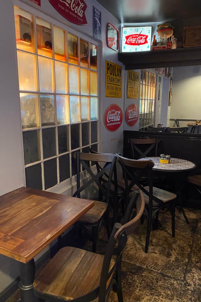 Wooden tables and chairs inside Bardstown Burger with vintage Coca-Cola signs on walls.