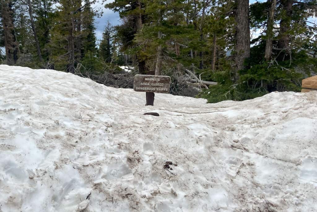 Snow packed several feet deep with sign warning that area is closed for dangerous cliffs.