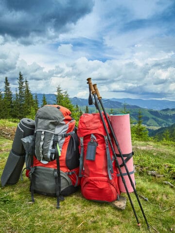 Two backpacks and trekking poles set on the ground overlooking mountains.
