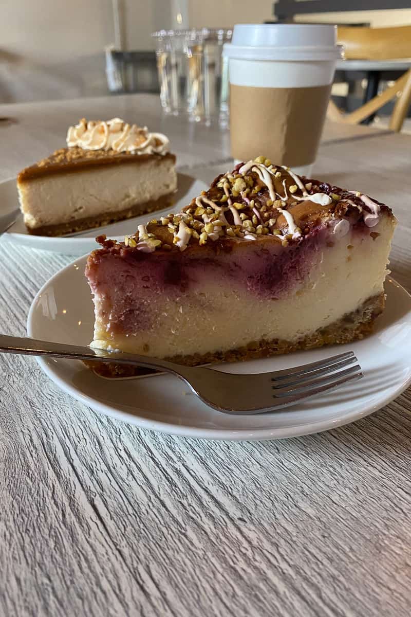 Slice of raspberry rose pistachio cheesecake with Biscoff cheesecake in background.