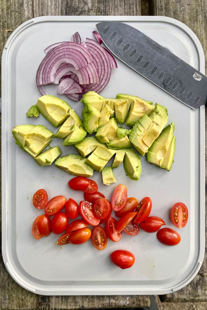 Sliced tomatoes, avocado, and red onion on cutting board.