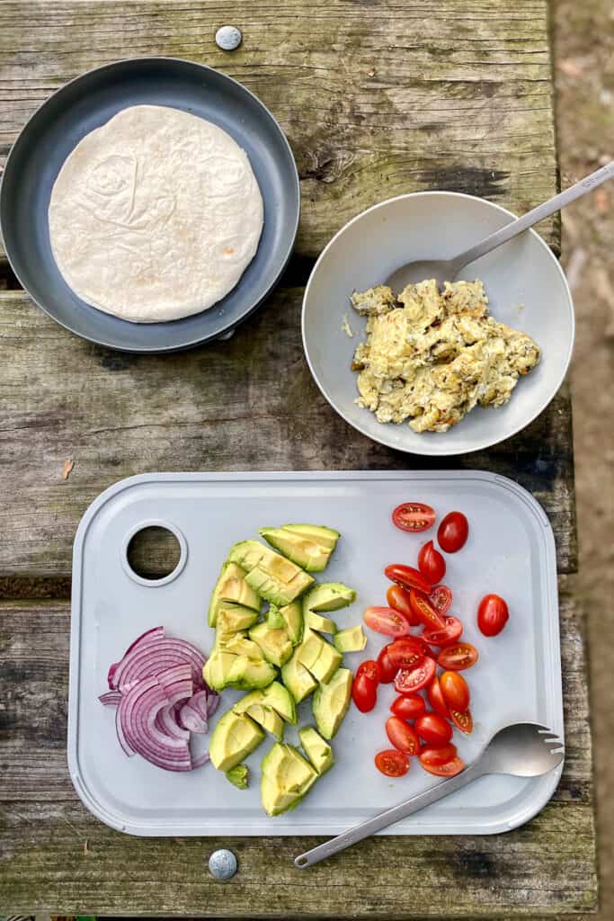 Bowl with tortillas, bowl with cooked eggs, and cutting board with chopped vegetables.