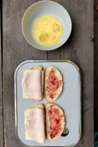 Slices of bread with cheese, meat, and jam next to bowl of egg mixture.