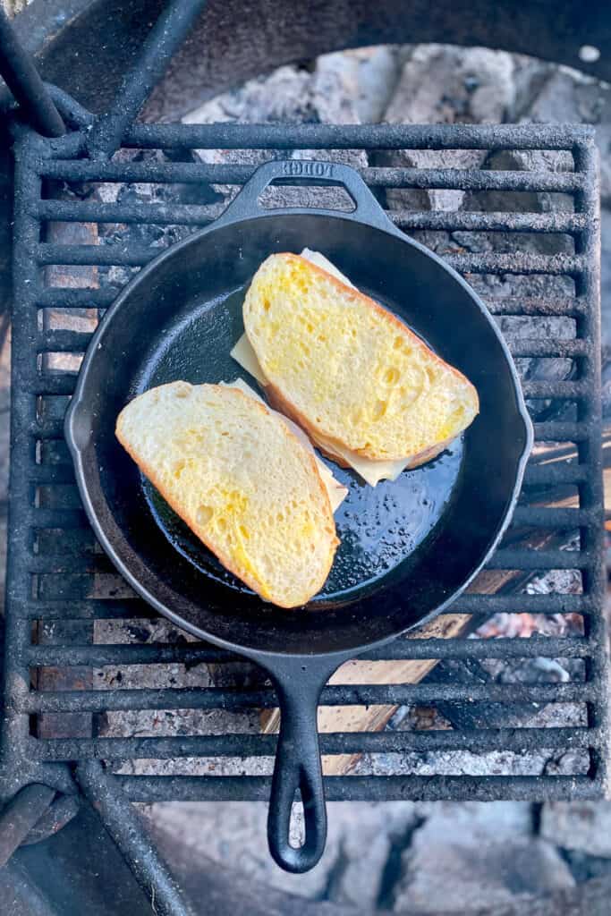 Monte cristo sandwiches cooking in cast-iron pan over campfire.