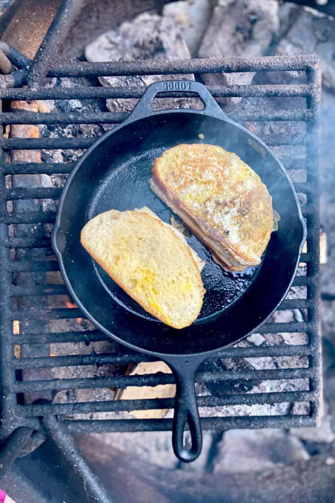 Monte cristo sandwiches in cast-iron pan, with one of them flipped to show a cooked golden side.
