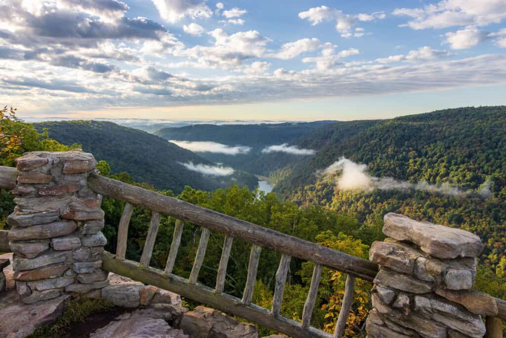 Wooden railings and rock pillars at overlook of river cutting through valley.