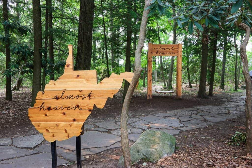 Wooden sign in the shape of West Virginia with "almost heaven" burned into it and a tree swing in background.