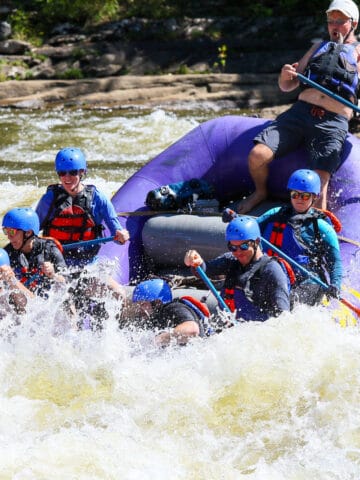Rafters navigating whitewater on Gauley River, with boat tipping downwards into the spray.