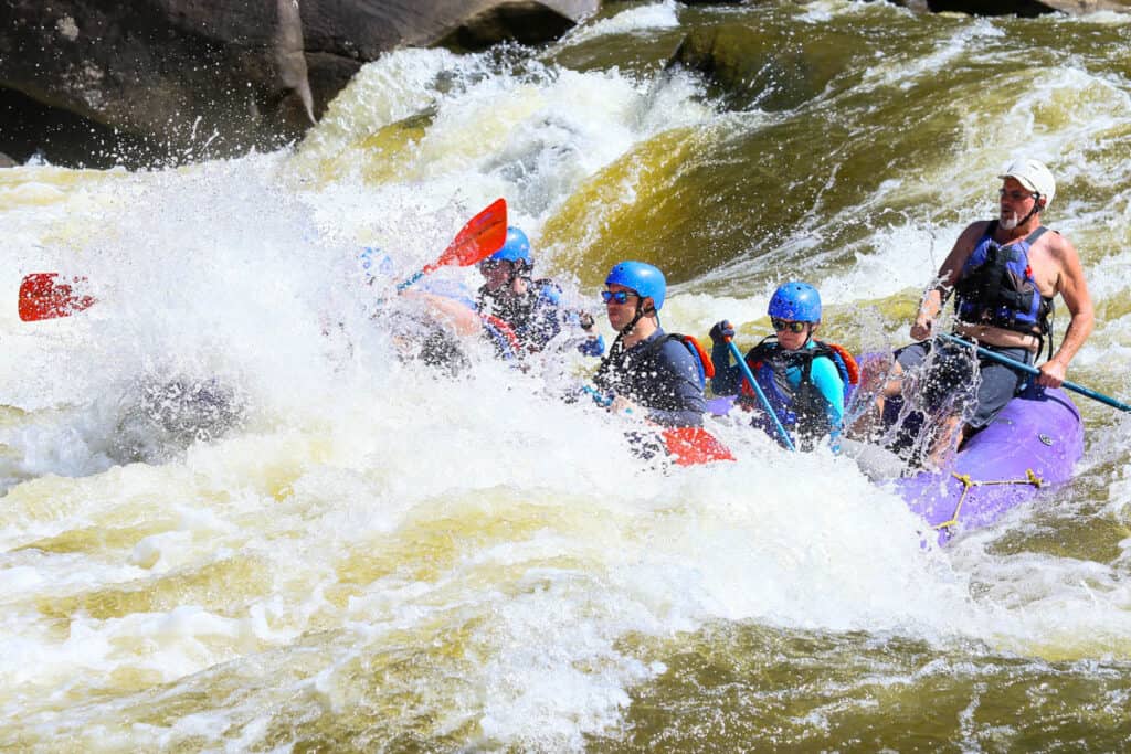Rafters navigating whitewater on Gauley River, with boat halfway covered in spray.