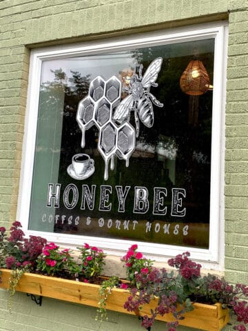 Window with logo for Honeybee Coffee and Donut House painted and flowers in windowbox beneath.