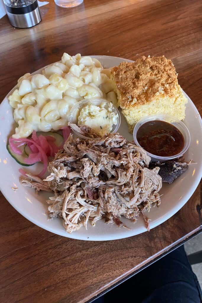 Pulled pork, barbeque sauce, corn grits bread, and macaroni and cheese on plate.